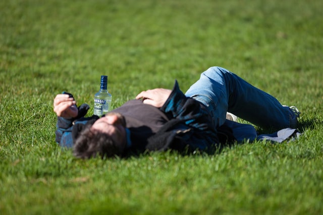 man laying on the ground with an empty bottle of smirnoff next to him